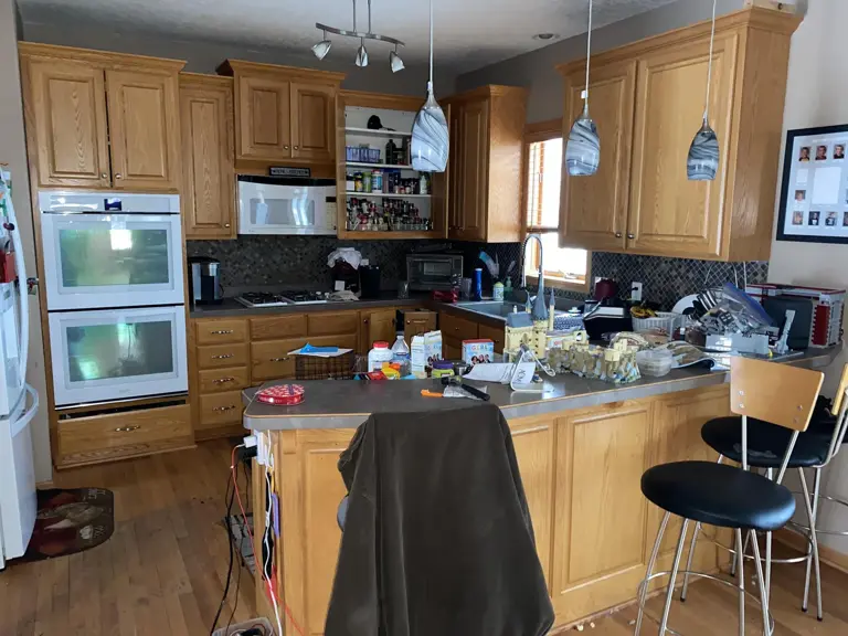 Dated oak kitchen with a laminate peninsula, bar stools, and mosaic tile backsplash before fire damage restoration