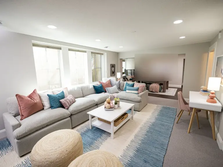 The same basement finished as a teen hangout with a large sectional, a patterned blue rug, and a study desk, opening to a raised alcove at the back