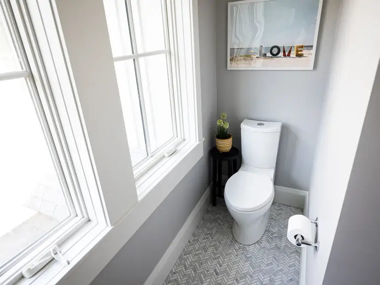 The same toilet room finished with herringbone marble floor tile, a new toilet in the corner, and the window to the left