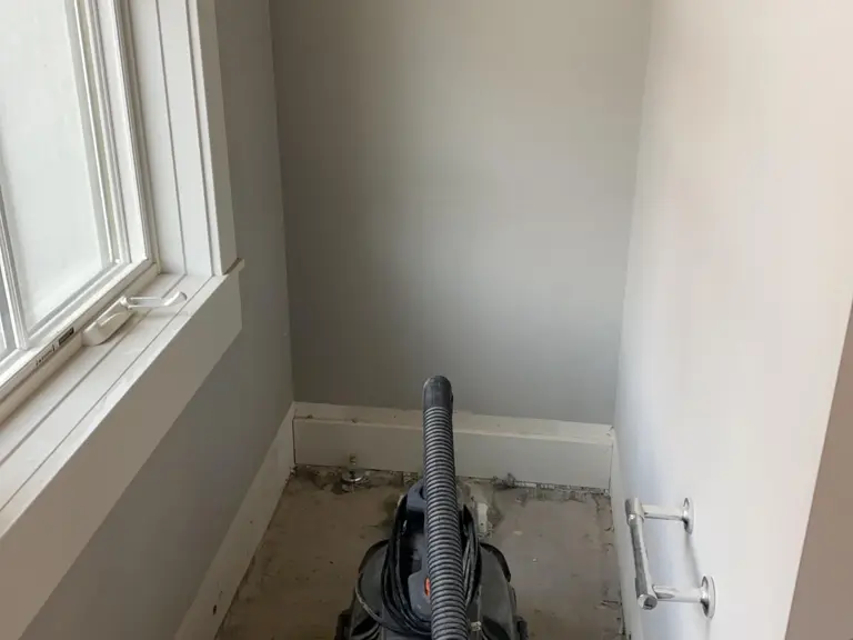 Upstairs toilet room stripped to the subfloor during water damage restoration, a shop vacuum where the toilet had been removed and a window to the left