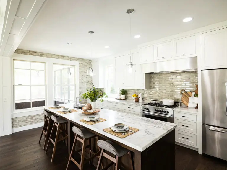 The same kitchen finished with white cabinetry, a marble-topped island with wood stools, a stainless range, and new dark hardwood floors