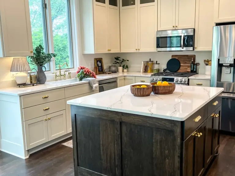 The same kitchen rebuilt with cream cabinets to the ceiling, quartz counters, and a dark stained island