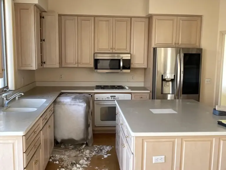 Original pickled oak kitchen with a wall microwave, white range, and insulation debris on the floor after the electrical fire