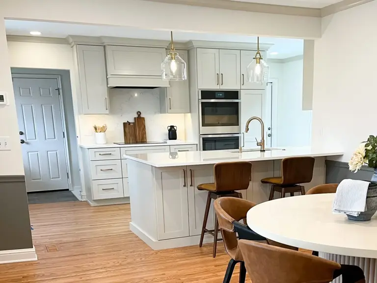 The same cooking wall rebuilt with greige shaker cabinetry, a vented hood over the cooktop and the wall ovens moved alongside it, with the entry door repainted grey