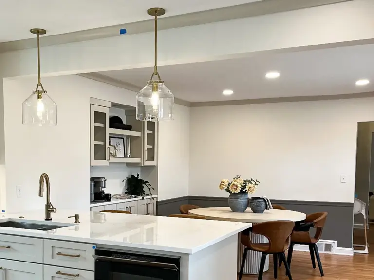 The same opening finished, with a quartz island, glass pendants and a built-in beverage station looking through to the dining room under the new beam