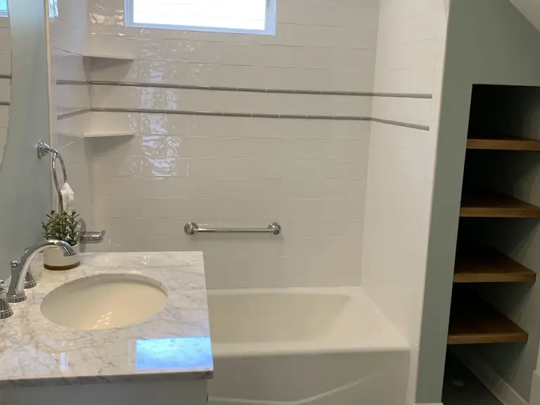 The same dormer bath finished in white subway tile with a marble-topped vanity, a tub and shower, and built-in wood shelving