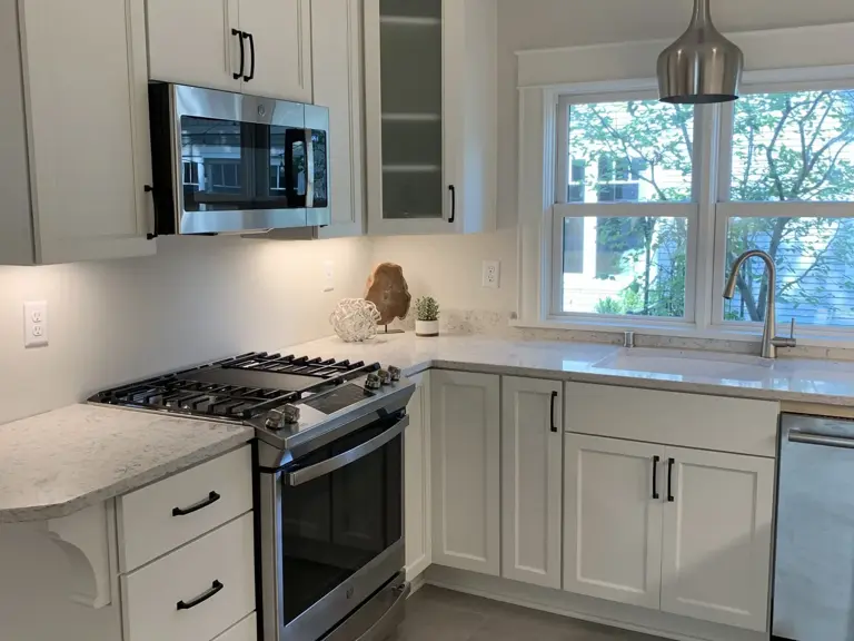 The same wall rebuilt with a stainless gas range and white cabinetry, the sink relocated under the window to the right