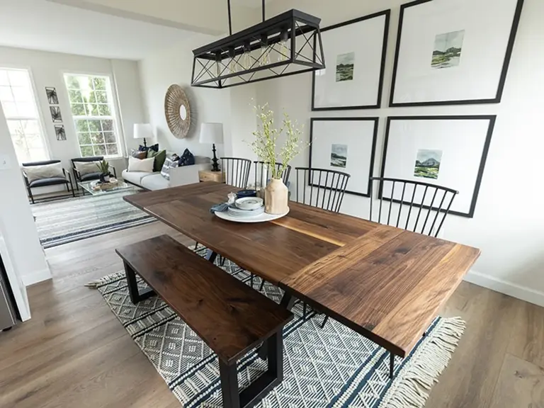 The same dining space with a walnut table and bench, a black linear chandelier, and a gallery wall, opening to the living room