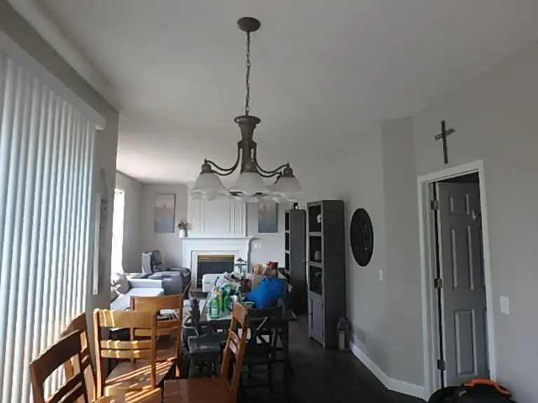 Cluttered dining area under a dated chandelier before restoration, with the fire-damaged living room and fireplace visible beyond