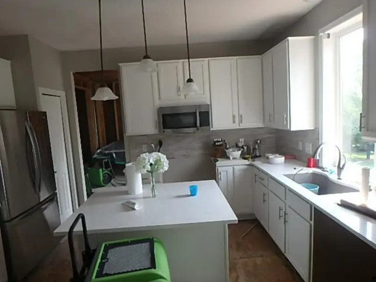 Soot- and water-damaged kitchen with white cabinets, an over-range microwave, and drying equipment on the floor after a lightning-strike fire