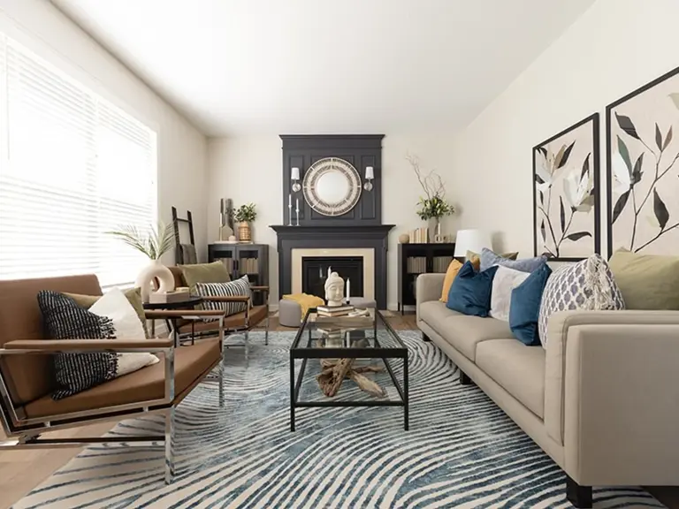 The same living room refreshed with a dark navy fireplace, a round mirror, and new furnishings under the vaulted ceiling