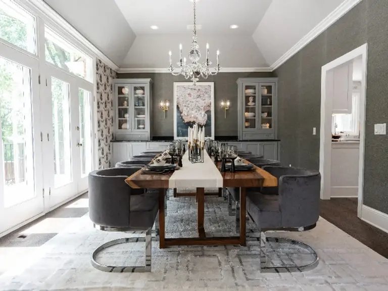 The same dining room with grasscloth walls, glass-front cabinets, a set table, and a chandelier beneath the vaulted ceiling after restoration