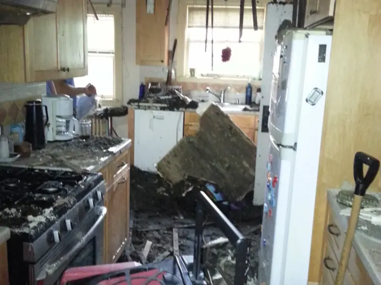 Fire-damaged kitchen with charred cabinets, soot-covered counters, and collapsed ceiling material before restoration