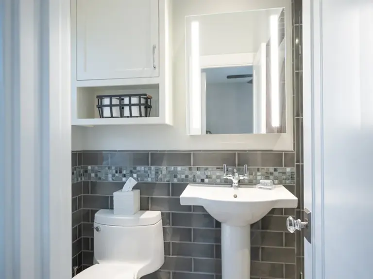 The same powder room rebuilt with grey tile, a glass mosaic band, and a new pedestal sink