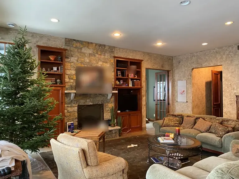 Great room before restoration, with a floor-to-ceiling stone fireplace flanked by dark wood built-ins and dated upholstered furniture