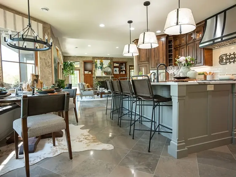 The same kitchen rebuilt with a grey island and barstools, a strapped-metal hood, and cherry cabinets, opening to the great room beyond