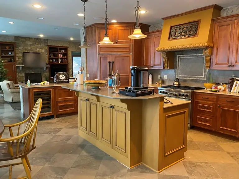 Dated Plymouth kitchen before water damage restoration, with a mustard-painted island, an ornate wood range hood, and cherry cabinets seen from the breakfast area