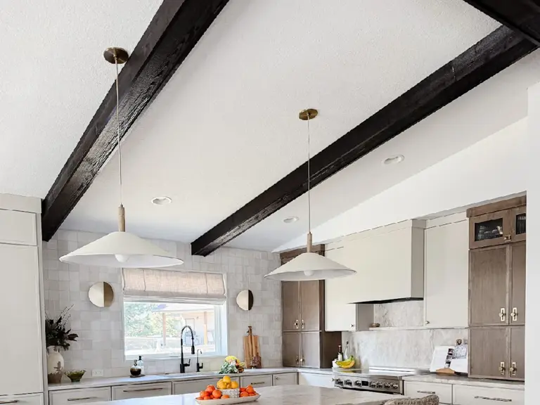 The same kitchen rebuilt with a large island, rattan stools, and custom cabinetry under the same vaulted ceiling and beams