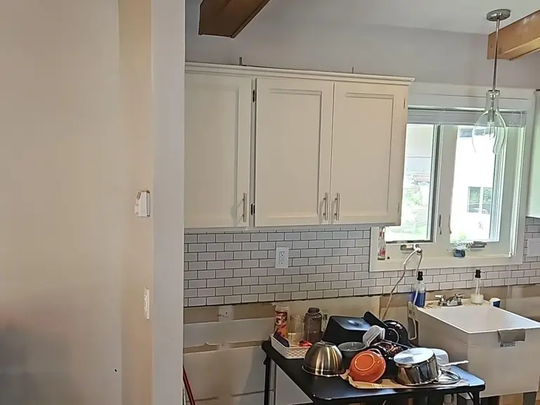 Original farmhouse sink under the kitchen window with white cabinets and subway tile before restoration