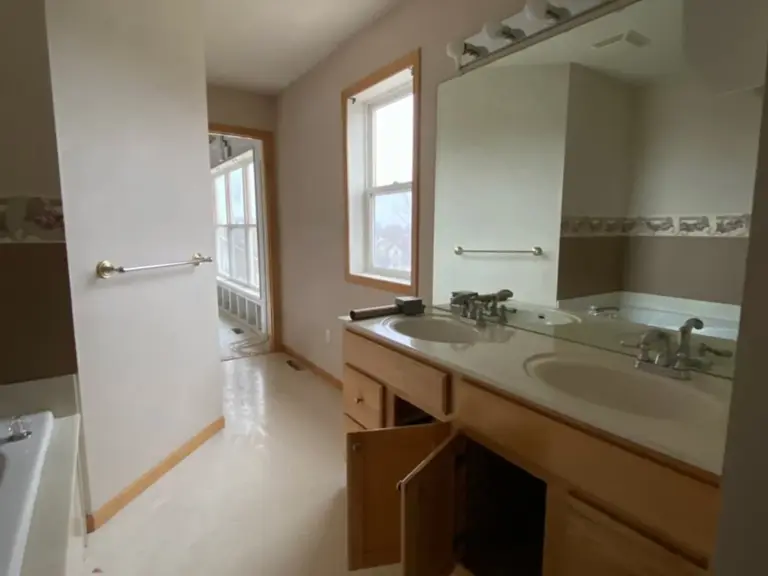 Original primary bathroom with an oak double vanity, frameless mirror, and floral wallpaper border before fire restoration