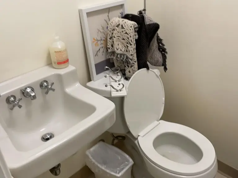 Dated basement bathroom before sewer backup restoration, with an old wall-hung sink, separate hot and cold taps, and plain cream walls