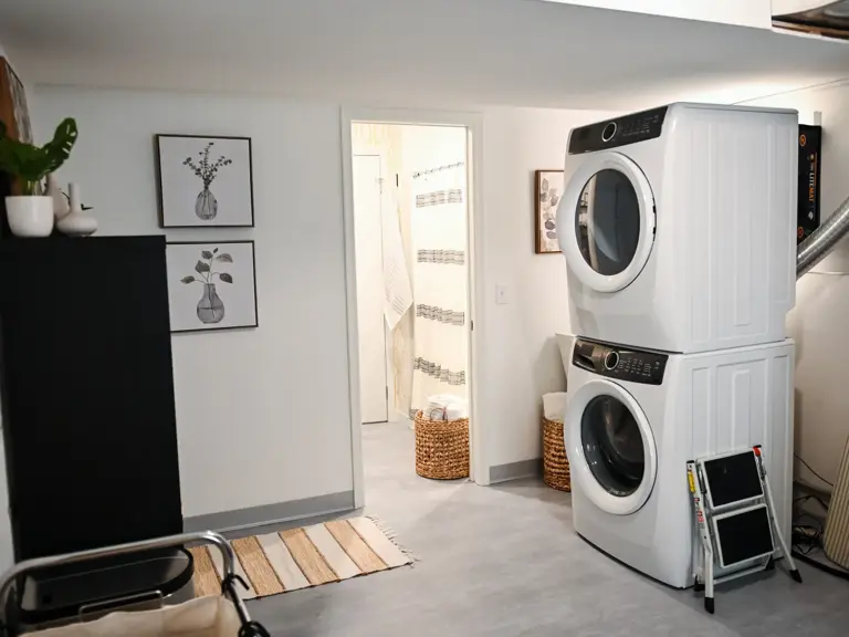 The same basement laundry area after restoration, with light gray plank flooring, finished walls, and a doorway opening to the rebuilt bathroom
