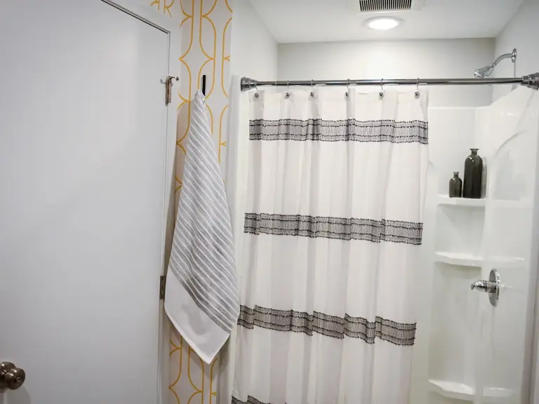 The same shower alcove with a new white shower surround, built-in corner shelves, and a striped curtain after basement restoration