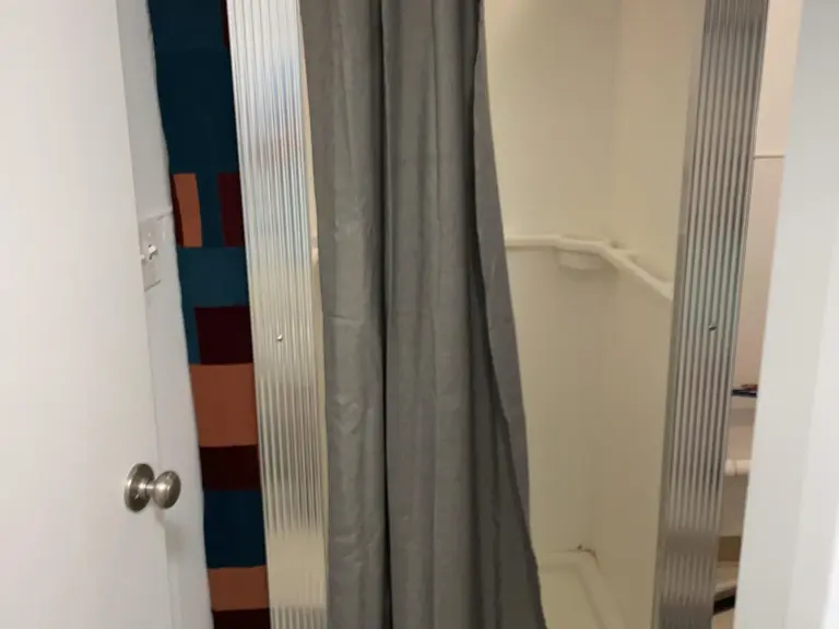 Narrow basement shower stall before restoration, with a corrugated panel surround and a fabric shower curtain