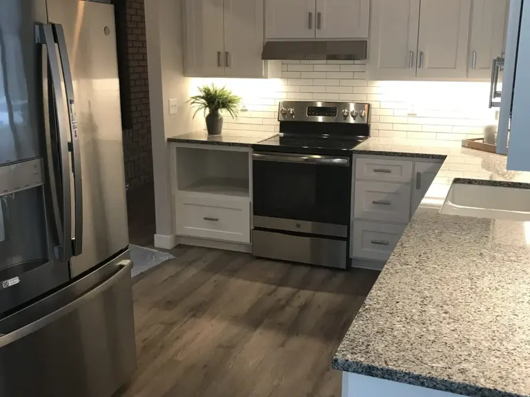 The same wall rebuilt with a stainless range, white cabinetry, and granite counters
