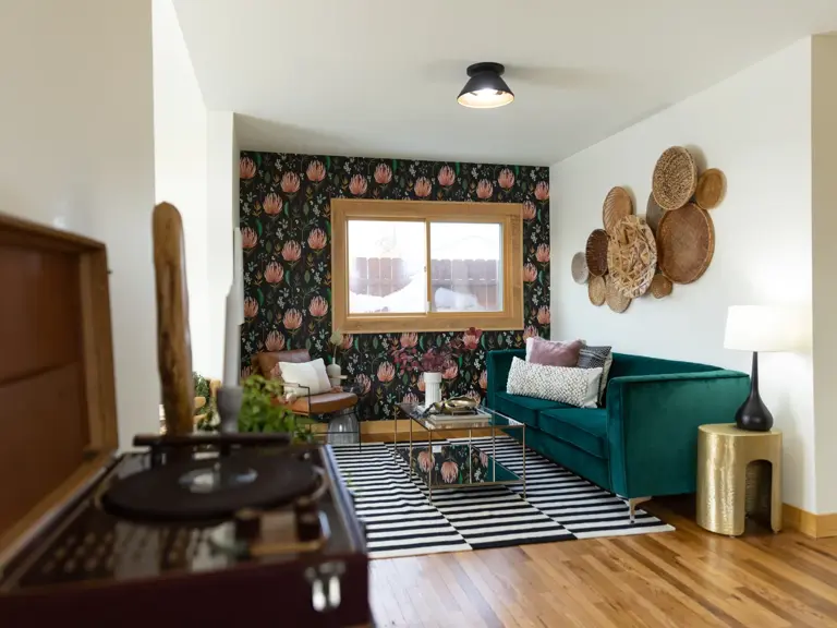 The same wall finished with bold botanical wallpaper, a wood-trimmed window, and a teal velvet sofa after restoration