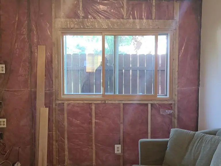 Living room wall stripped back to studs and vapor barrier around the window during water damage repairs