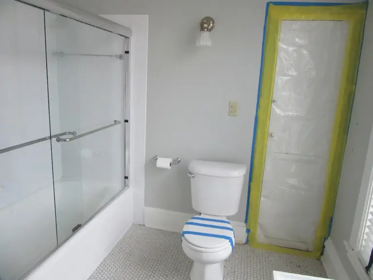 The original bathroom with a sliding glass tub enclosure and a doorway sealed for containment during restoration