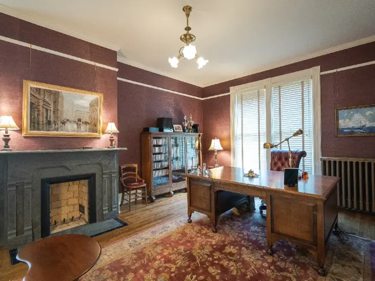 The same fireplace restored in a finished study with patterned walls, a period desk, and original woodwork