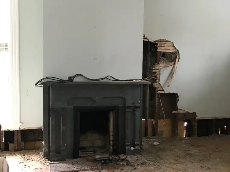 One of the home's custom fireplaces after the fire, with the wall beside it torn open and debris across the floor