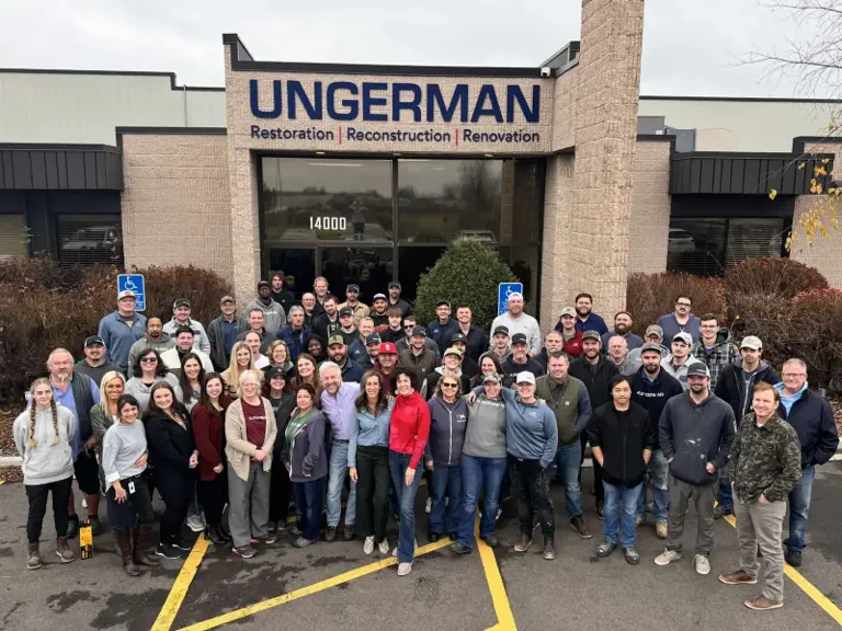 The full Ungerman team gathered outside the company office beneath the Ungerman Restoration, Reconstruction, Renovation building sign.