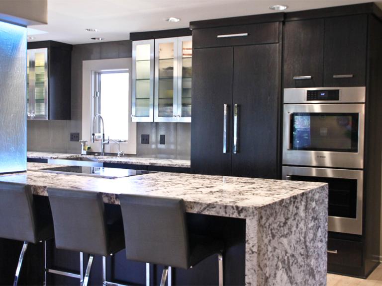 Modern kitchen with dark wood cabinetry, marble countertops, and stainless steel appliances. Four sleek barstools line the kitchen island.