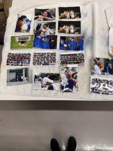 A collection of photos on a white towel includes various scenes: people hugging, graduation moments with blue caps and gowns, small collage prints with vibrant images. The atmosphere is joyful and celebratory. Ungerman Photographic Restoration Experts.