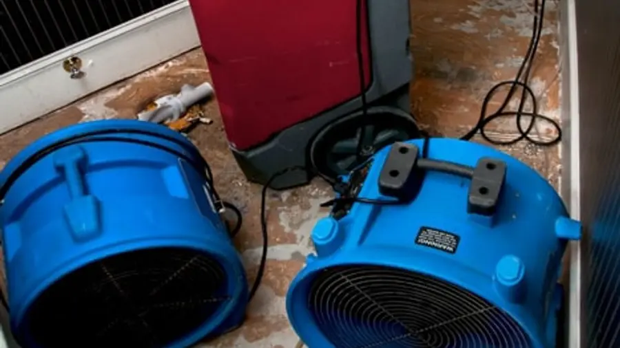Blue air movers and a red dehumidifier drying a room with water-damaged walls