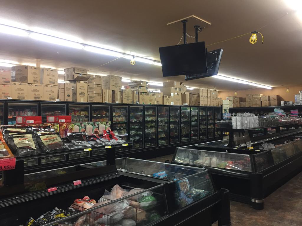 Grocery store interior with stocked refrigerated shelves and open coolers filled with various packaged foods. Boxes are stacked overhead. Bright lighting. Ungerman Construction, Prior Lake, MN