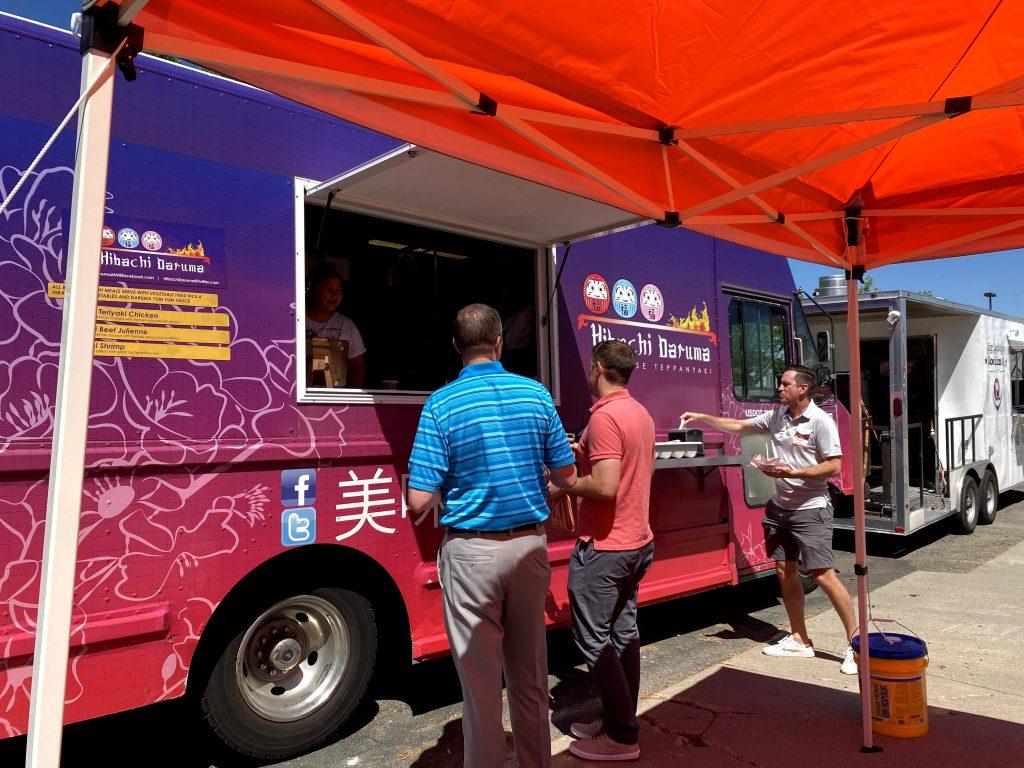 People gather at a vibrant purple food truck under a bright orange canopy, creating a lively and casual outdoor dining atmosphere.
