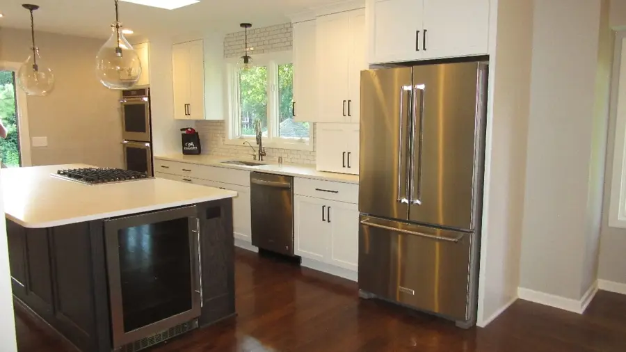 Modern kitchen with stainless steel appliances, white cabinetry, and a center island. Large windows provide natural light, creating an airy feel.