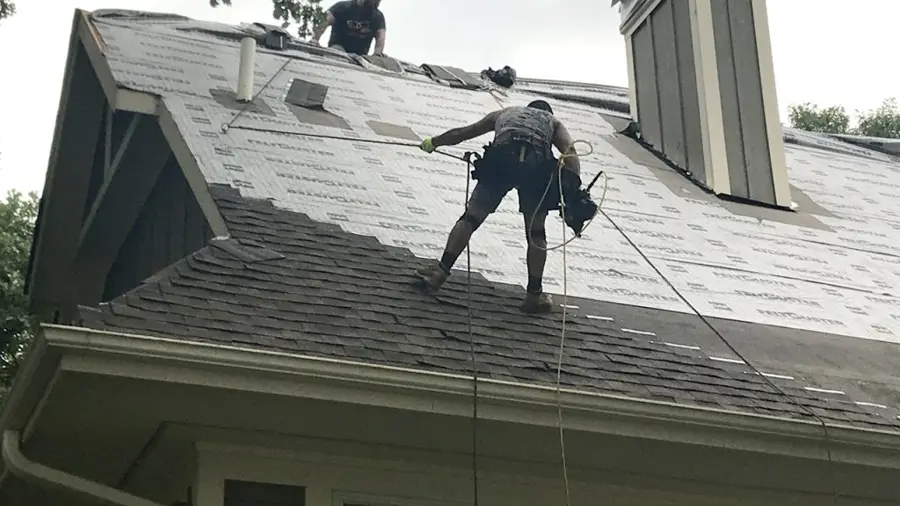 Two Men working on steep roof add new shingles