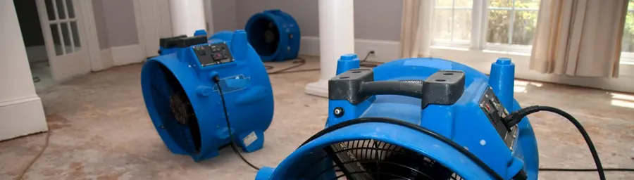Two blue industrial fans drying a water-damaged floor. Cords are scattered, indicating recent flooding cleanup.