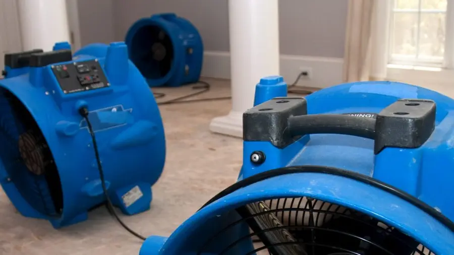 Two blue industrial fans drying a water-damaged floor. Cords are scattered, indicating recent flooding cleanup.