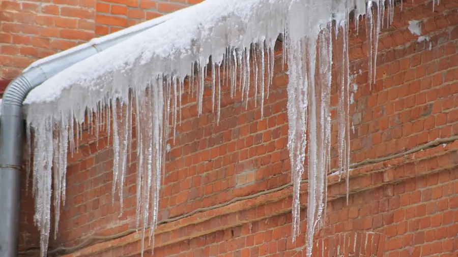 Long icicles hanging from a roof edge above a brick wall
