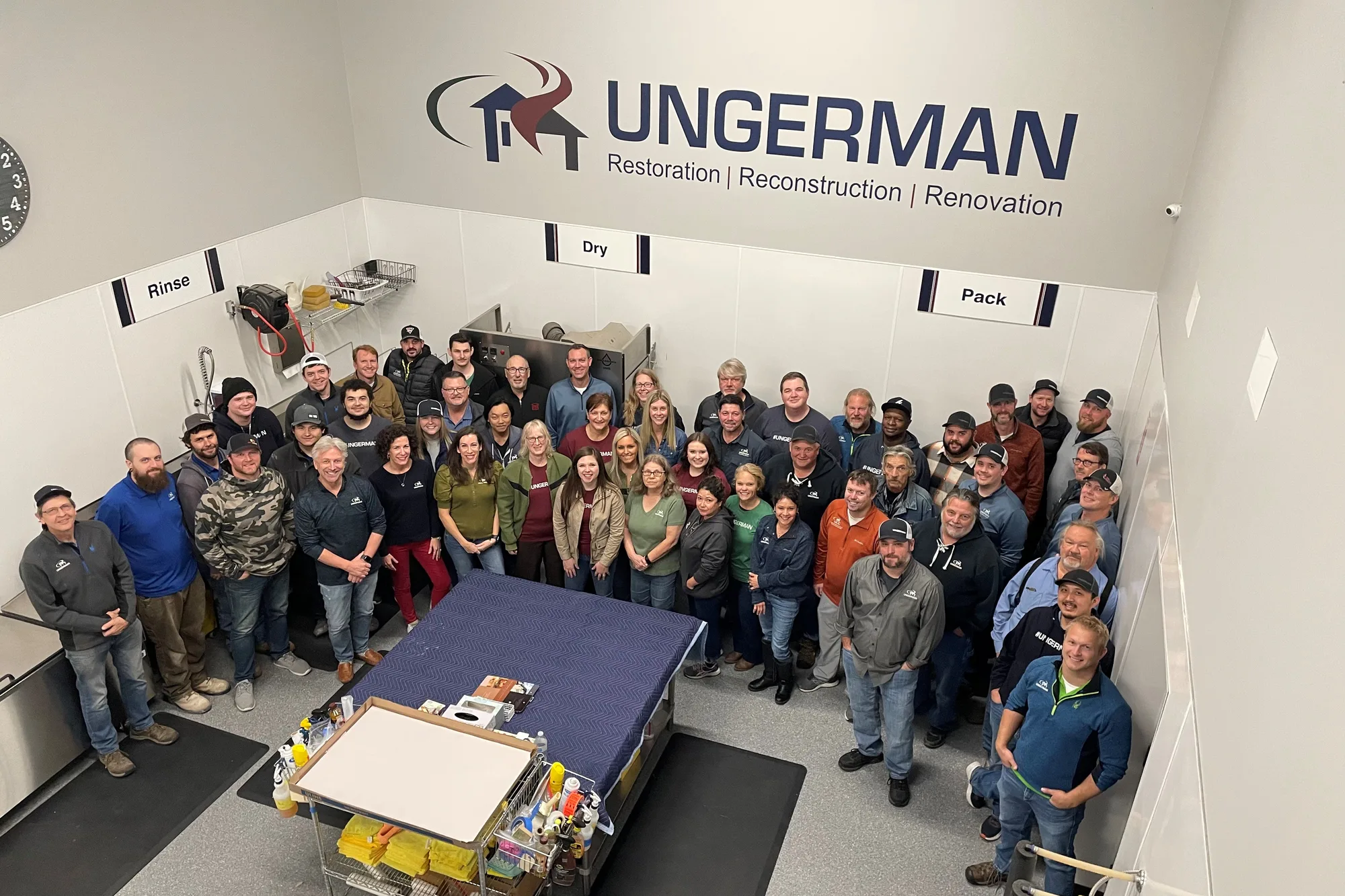 The Ungerman team gathered in the contents cleaning facility beneath the Ungerman Restoration, Reconstruction, Renovation wall sign